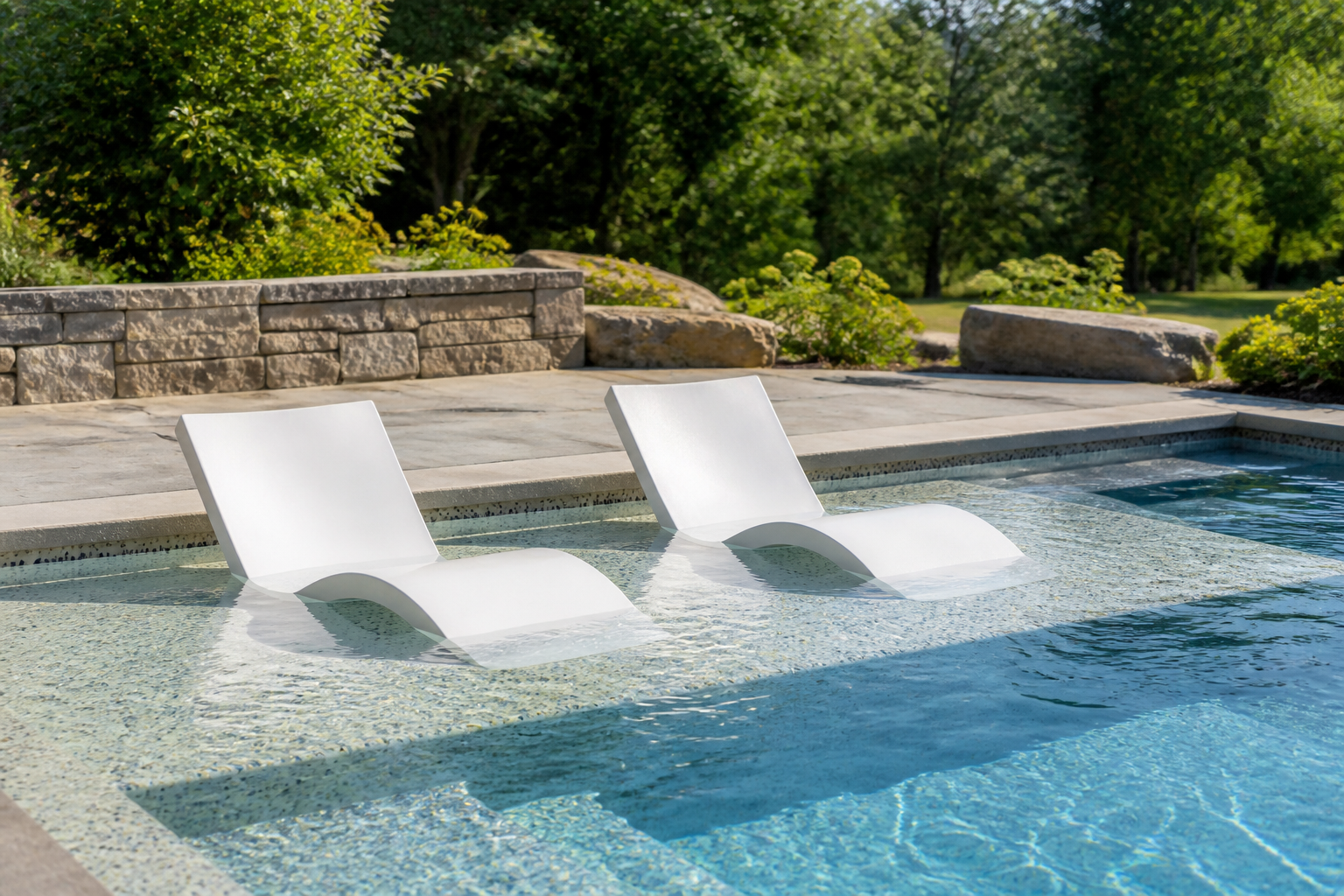 A luxury pool's tanning ledge with in-water lounge chairs, viewed from the stone patio on a sunny day in Ontario.
